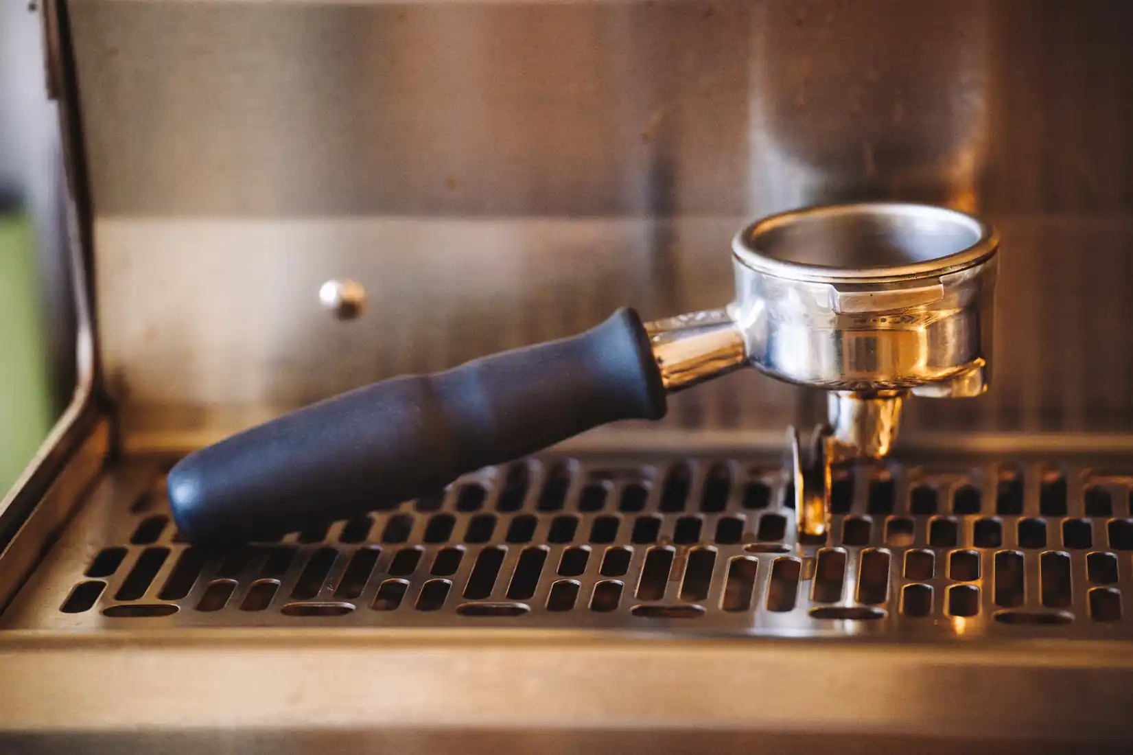 A stainless steel portafilter resting on the drip tray grate of an espresso machine